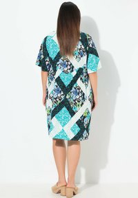 Lyhythihainen mekko, joka esittelee värikästä tilkkutöitä, jossa on kukka- ja geometrisia kuvioita sinisessä, vihreässä ja mustassa. Pehmeä rakenne, polvipituinen.