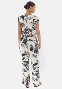 Kremowy kombinezon w kwiaty z czarnymi wzorami roślinnymi, z krótkimi rękawami, luźnym krojem i szerokimi nogawkami. Gładka tekstura oraz dopasowana talia.