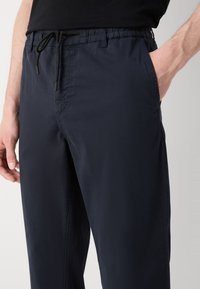 Marinblå byxor gjorda av lättviktigt tyg, med ett elastiskt midjeband, snörning och sidofickor. Slät textur med minimal sömnad.