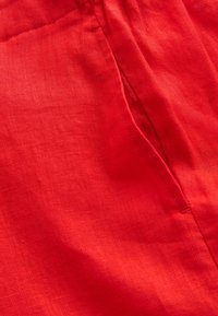 Gros plan d’un tissu rouge avec une couture visible et un tissage texturé, montrant des points détaillés et des plis.