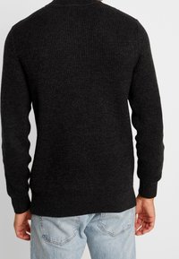 Schwarzer, gerippter Strickpullover mit langen Ärmeln und Rundhalsausschnitt, strukturierter Stoff, kombiniert mit hellblauen Jeans.