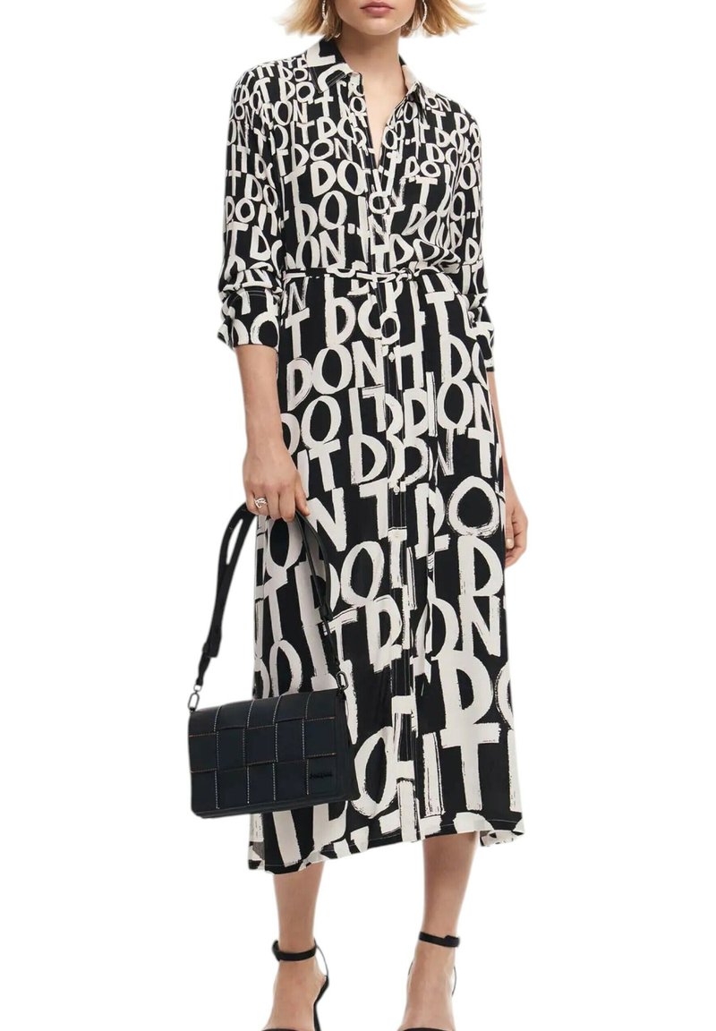 Abito lungo in bianco e nero con un audace motivo testuale, colletto, chiusura con bottoni sul davanti e vita con cintura; abbinato a una borsa a tracolla nera testurizzata.