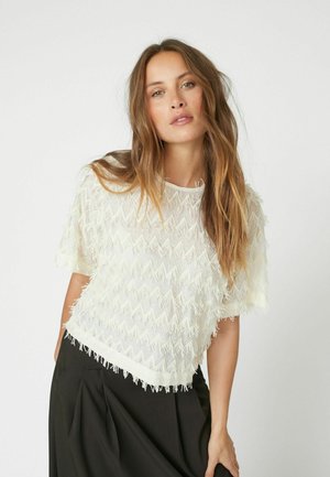 White fringe top with a zigzag pattern and short sleeves, featuring a textured design and a loose fit, paired with black bottoms.