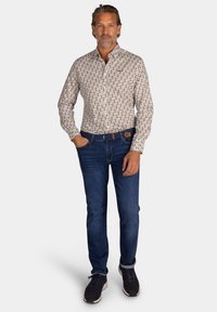 Witte blouse met een bruin bloemenpatroon, met een knoopsluiting op de kraag, gecombineerd met donkerblauwe spijkerbroek en donkere sneakers. Gladde stof, relaxte pasvorm.