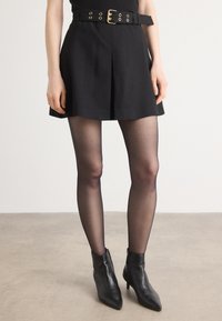 Svart mini skjørt med plisseringer, med et bredt belte med gullspenne. Modellen har på seg svarte, gjennomskinnelige strømpebukser og spisse ankelstøvler.