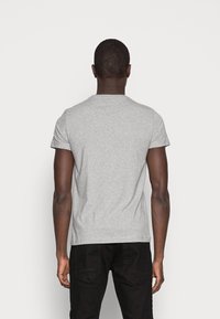 T-shirt grigio a maniche corte in cotone, con colletto rotondo classico e un design aderente, abbinato a pantaloni neri.