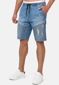 Shorts en denim avec une taille à cordon de serrage, couleur bleu clair, légères distorsions et sections en texture côtelée sur les côtés.