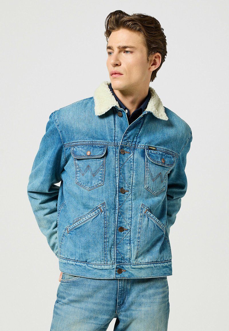 Giacca in denim azzurro chiaro con colletto in shearling, dotata di chiusura a bottoni, due tasche sul petto e dettagli usurati.