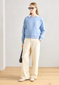 Sweatshirt cropped bleu clair avec un col blanc, associé à un pantalon large crème et des ballerines nude. Lunettes de soleil noires et petit sac noir inclus.