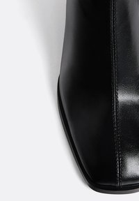 Schwarze Leder-Ankle Boot mit spitzer Zehe, glatter Textur, vertikaler Nahtdetails und einer niedrigen schwarzen Sohle.