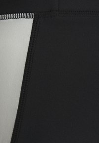 Melnas sporta šortus ar gludu tekstūru, kuriem ir gaismas pelēka sānu paneļa un kontrastējoša balta diega šuvju garumā.