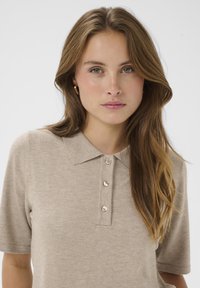 Polo en maille beige à manches courtes, col à revers et devant boutonné avec quatre boutons assortis. Texture lisse.