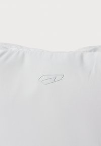 Weißes Kissen mit glatter Stoffoberfläche, das oben in der Mitte ein dezentes, geprägtes Logo aufweist und so ein minimalistisches Design schafft.