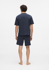 Tamnoplava pamučna majica kratkih rukava, u kombinaciji s odgovarajućim šorcem. Jednostavan dizajn, meka tekstura i opušteni kroj.