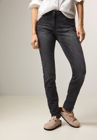 Jeans skinny de mezclilla negra con sutiles desgaste y decoloración, combinados con zuecos de ante beige con herrajes decorativos.