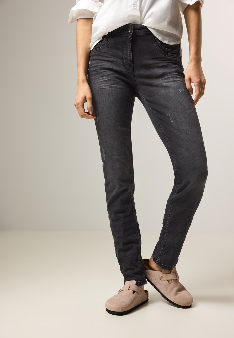 Musta farkku skinny jeans vaimealla kulutuksella ja haalistumalla, yhdistettynä beigeihin mokkanahkakenkiin, joissa on koristeellista metalliosaa.