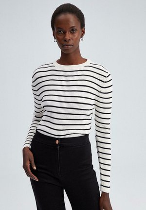 Schwarz-weiß gestreifter, gerippter Pullover mit Rundhalsausschnitt und langen Ärmeln, kombiniert mit hoch taillierten schwarzen Hosen.