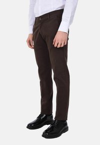 Chino marroni realizzati in cotone, con una vestibilità regular, dotati di tasche frontali e chiusura con bottone, abbinati a scarpe eleganti nere e lucide.