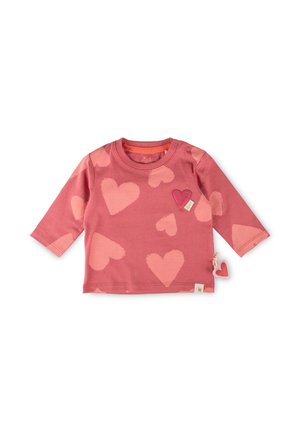 Maglietta rosa a maniche lunghe per neonati con grandi stampe di cuori rosa chiaro e una piccola patch a forma di cuore cucita vicino allo scollo su sfondo bianco.