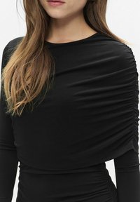 Czarna bluzka z długim rękawem z marszczonym materiałem na ramionach i bokach, wykonana z gładkiego, elastycznego materiału. Dobrze dopasowana do ciała.