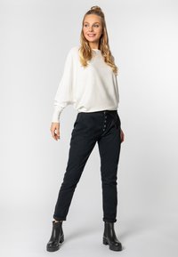 Overgroot crèmekleurig sweater met een ronde hals, gecombineerd met slim fit zwarte broek met knoopsluiting en opgerolde manchetten, aangevuld met zwarte enkellaarsjes.