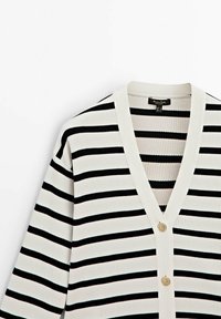 Black and white striped cardigan with ribbed texture, V-neck, and three gold-tone buttons down the front. Soft fabric and relaxed fit.