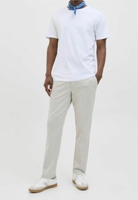 Bílý bavlněný tričko, světle šedé kalhoty, modrá bandana kolem krku, bílé tenisky s hnědými akcenty, minimalistický design.