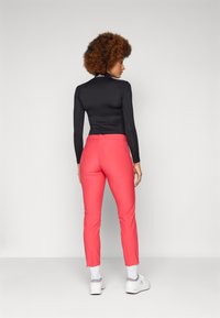 Fitted black long-sleeve top and bright pink tapered pants, designed with a smooth texture and simple construction, paired with white sneakers.