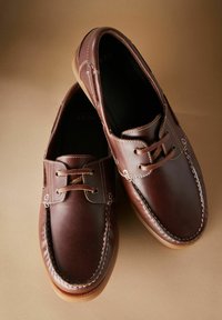 Braune Lederschuhe mit Schnürdesign, featuring weiße Nähte und einer runden Zehenpartie. Gummisohle und weiche Innenauskleidung.