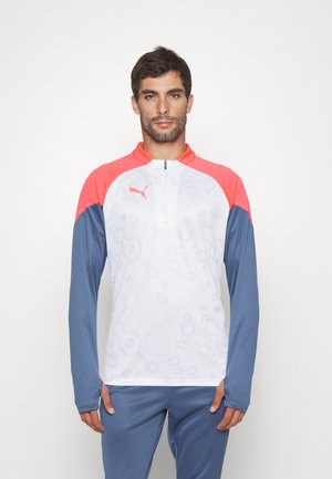 Langsleeve sporttop met een witte body, koraalrode schouders en blauwe mouwen. Het heeft een kwart-rits aan de voorkant en een subtiel patroon.