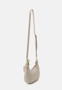 Beige quiltad handväska med en böjd form, justerbar rem, guldfärgade detaljer och dragkedjestängning. Slät textur med en liten storlek.