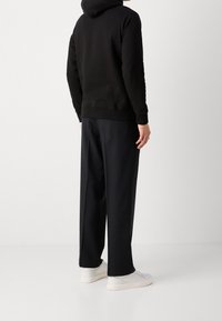 Sudadera negra con capucha de corte relajado, combinada con pantalones oscuros y sueltos. Zapatillas blancas completan el conjunto. Textura de tela suave.