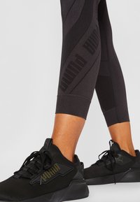 Czarne legginsy sportowe z teksturowanym wzorem oraz logo PUMA. W zestawieniu z eleganckimi czarnymi sneakerami z siateczkowymi i sznurowanymi detalami.