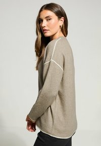 Beige Strickpullover mit lockerer Passform, der an den Nähten und an den gerippten Bündchen weiße Akzente aufweist. Weiche Textur und leicht übergroße Form.
