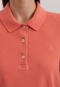 Koraalkleurig poloshirt van een textuurstof, met drie knopen en een geborduurd "MOP" logo op de borst, met een klassiek kraagontwerp.