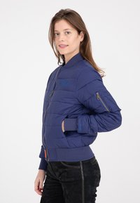 Giacca imbottita blu navy con chiusura a zip, polsi a coste e dettaglio del logo. Il design trapuntato e le tasche laterali ne aumentano la funzionalità.