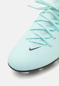 Crampon de football bleu clair avec une tige synthétique texturée, logo Nike noir et crampons blancs sur une semelle extérieure noire. Les lacets sont bien serrés.