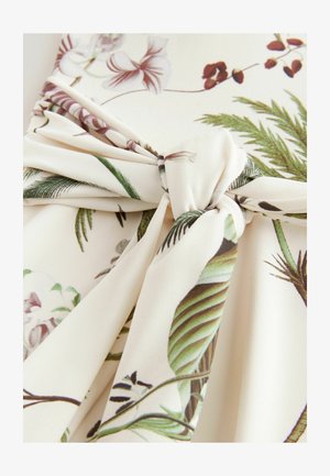 Materiał w kremowy wzór kwiatowy z zielonymi liśćmi i fioletowymi kwiatami. Tkanina jest miękka i ma związany detal na środku.