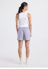 Valkoinen hihaton paita yhdistettynä purppuran- ja valkoisruudullisiin shortseihin, joissa on joustava vyötärönauha, sekä valkoiset nilkkasukat, joissa on oranssit raidat.