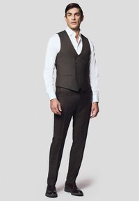 Brązowy garnitur w kratę z dopasowaną kamizelką z sześcioma guzikami oraz białą koszulą. Spodnie mają krojony fason i są zestawione z ciemnymi butami wizytowymi.