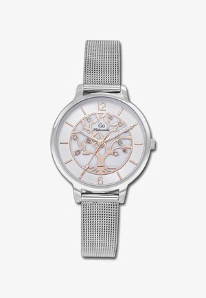 Montre en quartz argentée avec un bracelet en maille ; elle possède un cadran blanc, un design d'arbre, et des accents en or rose sur les index des heures et le contour de l'arbre.