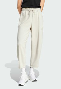Helle beige Sweatpants mit einem elastischen Taillenbund, Seitentaschen und dezentem Adidas-Logo. Mischgewebe aus Baumwolle, lockere Passform und gerippte Bündchen an den Knöcheln.