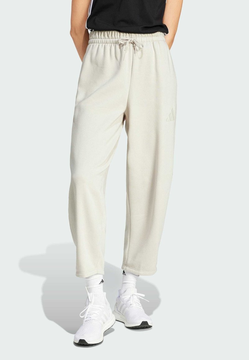 Helle beige Sweatpants mit einem elastischen Taillenbund, Seitentaschen und dezentem Adidas-Logo. Mischgewebe aus Baumwolle, lockere Passform und gerippte Bündchen an den Knöcheln.