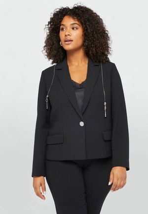 Zwarte op maat gemaakte blazer van soepel materiaal, met een zilveren kettingdetail op de schouder, een enkele knoop en twee voorzakken.