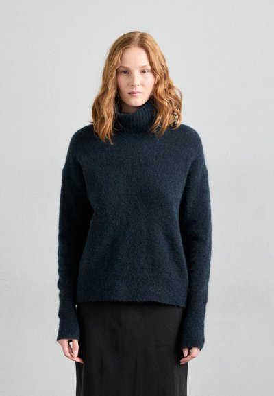Navy blue turtleneck sweater made of soft, textured knit. The design features long sleeves with extended cuffs and a relaxed fit.