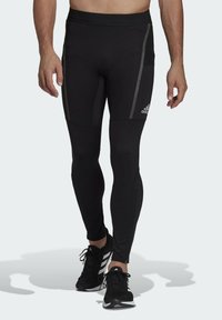 Leggings sportivi neri con un design aderente, caratterizzati da strisce laterali grigie e una vita sicura. Abbinati a scarpe sportive nere.