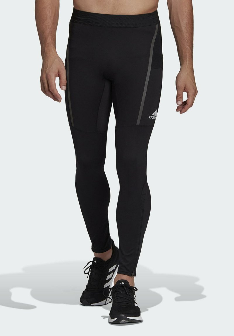 Leggings sportivi neri con un design aderente, caratterizzati da strisce laterali grigie e una vita sicura. Abbinati a scarpe sportive nere.