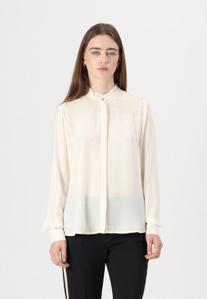 Cream blouse with a ruffled collar, textured detailing on shoulders, and button closure. Long sleeves and sheer fabric design.