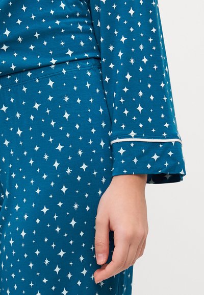 Conjunto de pijama turquesa com padrões de estrelas e flocos de neve brancos. Apresenta mangas longas com detalhes de punho, tecido suave e um ajuste confortável.