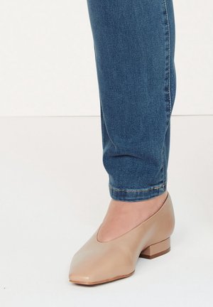 Beżowe buty na niskim obcasie z ostrym noskiem, wykonane z gładkiego materiału. Noszone z niebieskimi slim jeansami, prezentujące schludny, casualowy wygląd.